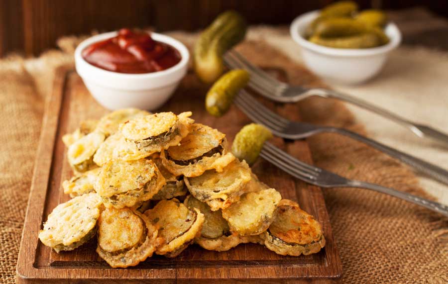 Fried pickles on a wooden board with fork and ketchup