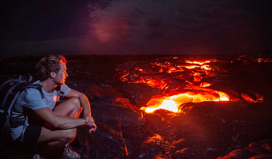 A man sitting while observing the lava flow at Kilauea Volcano