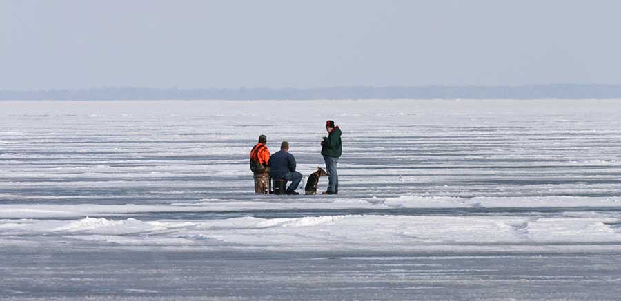 View of three people and a dog ice fishing in Michigan