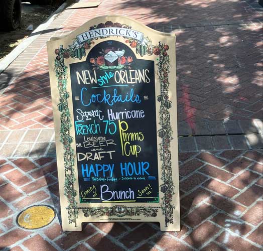 A sign on a sidewalk containing a cocktail menu